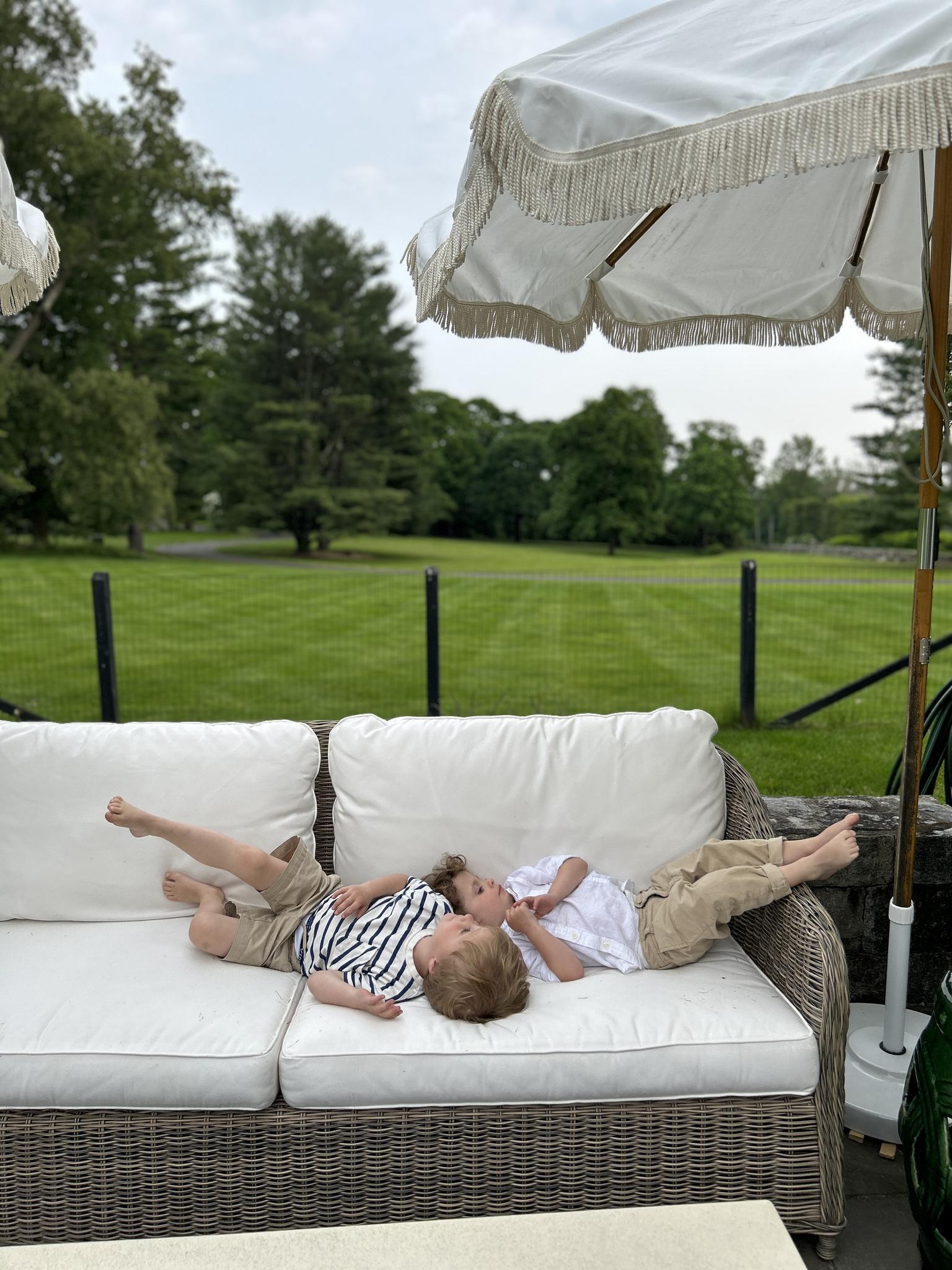 Boys playing on outdoor sofa with umbrella above